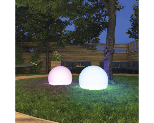 Deux sphères lumineuses dans un jardin de nuit, avec des arbres et des meubles de jardin en arrière-plan.