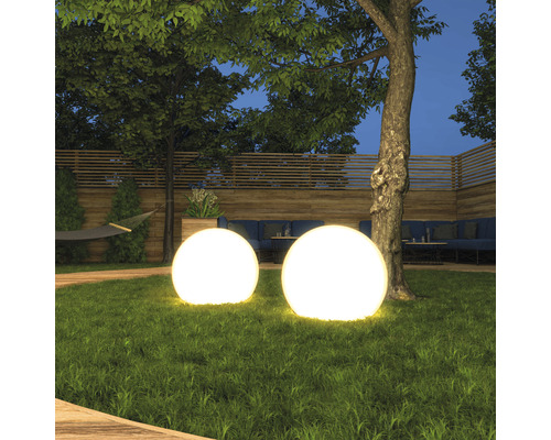 Deux sphères lumineuses dans un jardin avec pelouse, arbres et terrasse en bois.