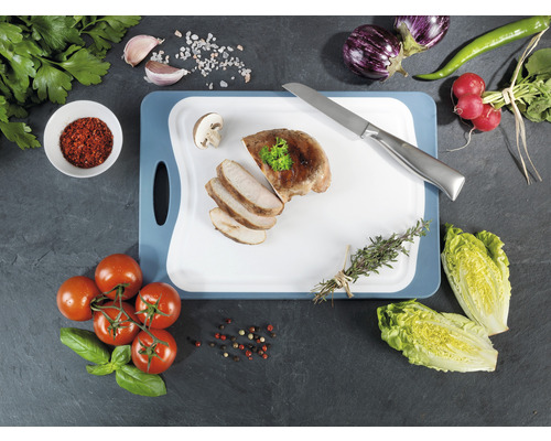 Zubereitete Mahlzeit mit Fleisch auf einem Schneidebrett mit Gemüse und Kräutern.