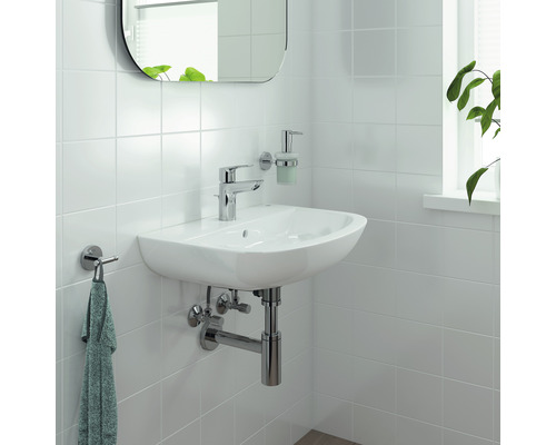 Lavabo mural blanc avec robinet, distributeur de savon et porte-serviettes dans une salle de bain lumineuse.