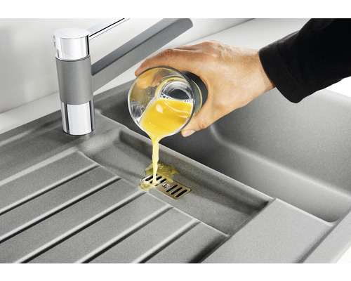 Spüle mit Wasserhahn und Hand, die ein Glas mit Flüssigkeit ausgießt