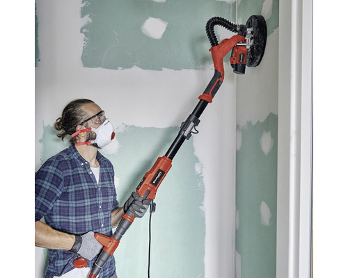 Un homme ponce un mur avec une ponceuse girafe