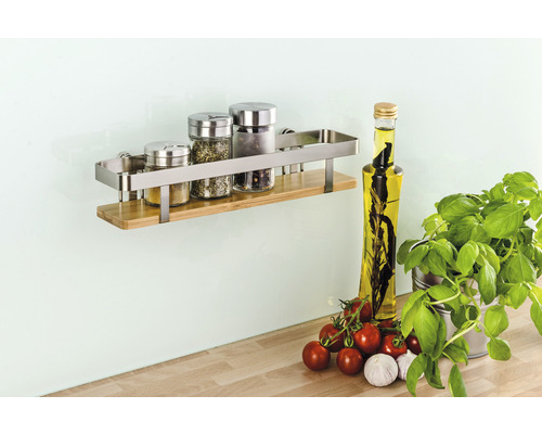 Wandregal aus Edelstahl und Holz mit Gewürzgläsern, Ölflasche, Tomaten, Knoblauch und Basilikum.