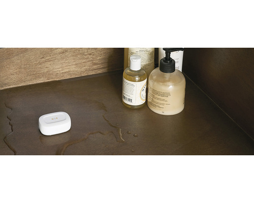 Scène avec des articles de toilette et un détecteur d''humidité blanc sur une étagère avec des résidus d''eau