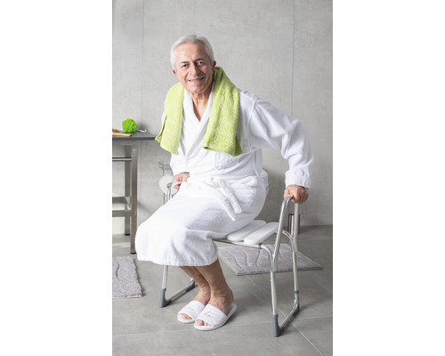 Ein Mann sitzt auf einem Duschstuhl mit Armlehnen im Badezimmer.