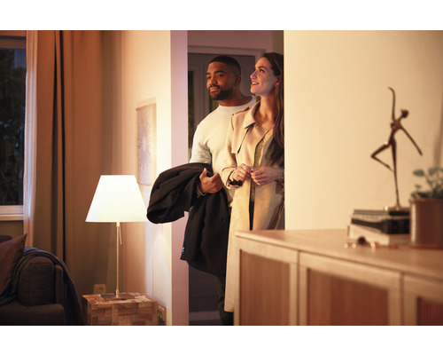 Paar betritt ein hell erleuchtetes, modern eingerichtetes Zuhause mit Tischleuchte.