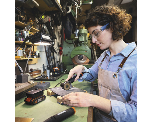 Une femme travaille avec une meuleuse à tronçonner sur une pièce dans un atelier. Des outils et un établi se trouvent à l''arrière-plan.