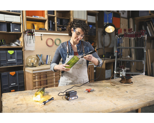 Femme travaille avec un outil multifonctionnel sur une bouteille en verre dans un atelier.