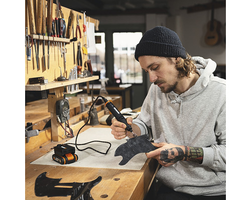 Un homme travaille une pièce avec un outil multifonction dans un atelier.