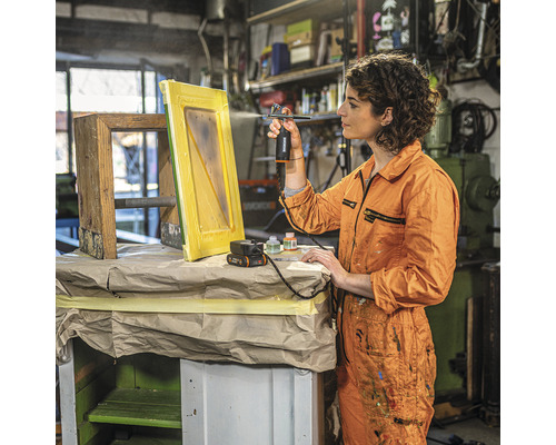 Une femme vaporise de la peinture avec un pistolet à peinture sur un cadre en bois dans un atelier.