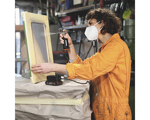 Femme utilisant un pistolet à peinture pour peindre un cadre de fenêtre