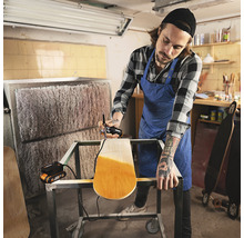 Mann lackiert ein Skateboard mit einer Farbspritzpistole in einer Werkstatt.