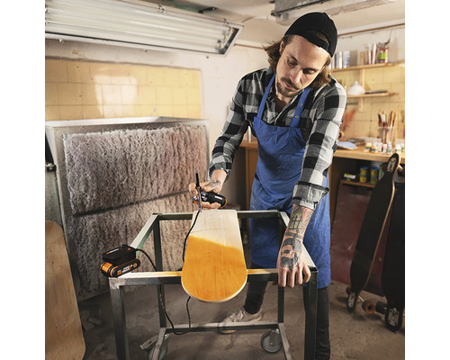 Un homme peint un skateboard avec un pistolet à peinture dans un atelier.