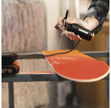 Eine Person benutzt eine Airbrushpistole von Worx, um ein Holzbrett zu bemalen.