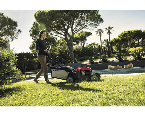 Frau bedient einen Honda Rasenmäher im Garten.
