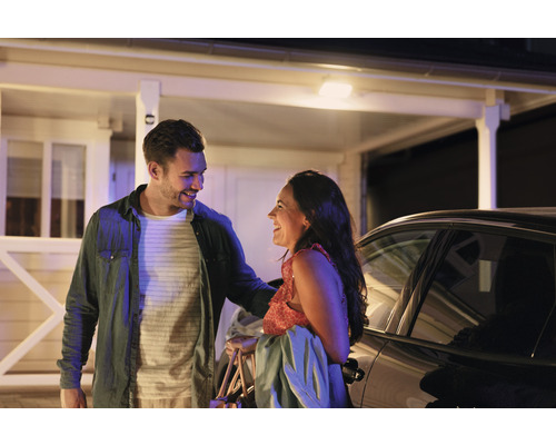 Ein Paar vor einem Haus und einem Auto lacht sich an.