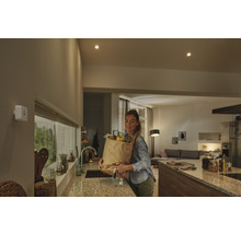 Weißer Bewegungsmelder an einer Wand in einer modernen Küche mit einer Frau, die eine Einkaufstüte trägt.