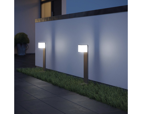 Zwei Gartenleuchten beleuchten einen Weg und eine Rasenfläche vor einer Wand.