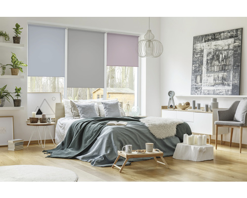 Chambre avec lit, commode et fenêtres avec stores enrouleurs de différentes couleurs.