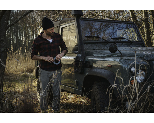 Homme avec du ruban adhésif à côté d''un véhicule tout-terrain sur le terrain.