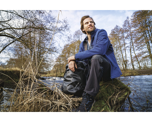 Un homme est assis avec un sac à dos au bord d''un ruisseau dans la nature.