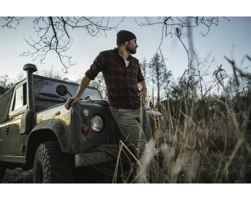 Homme en chemise à carreaux appuyé sur un véhicule tout-terrain dans un environnement naturel