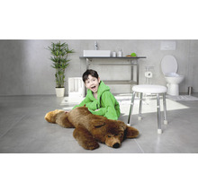 Salle de bains lumineuse avec un garçon en peignoir assis à côté d''un ours sur un tabouret, avec lavabo, toilettes et plante