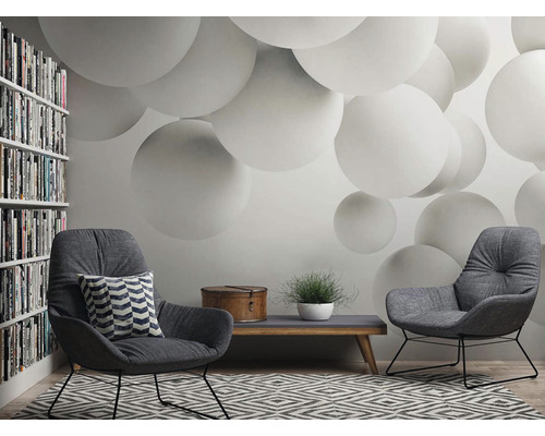 Salon avec deux fauteuils, une table basse, une bibliothèque et un papier peint à motif de sphères