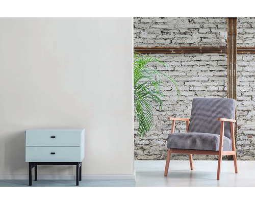 Wohnzimmer mit Sessel, Nachttisch und Zimmerpflanze vor einer Ziegelwand