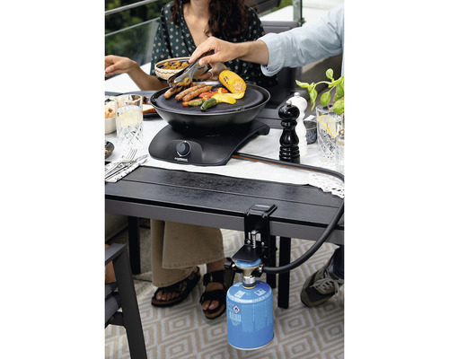 Szene mit einem Tischgrill, der an einem Tisch befestigt ist und von Personen beim Grillen verwendet wird.