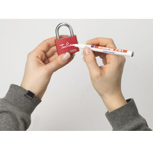Une personne écrit sur un cadenas rouge ABUS avec un marqueur de peinture Edding 751 blanc.