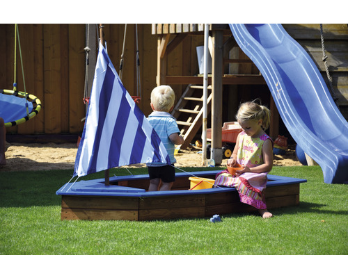 Des enfants jouent dans un bac à sable avec une voile sur une aire de jeux avec une tour de jeux et un toboggan