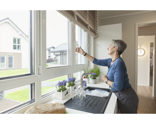 Frau öffnet ein Fenster in einer hellen Küche mit Spüle