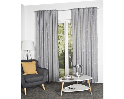 Salon avec fauteuil gris, table blanche et rideaux gris à motifs devant une fenêtre