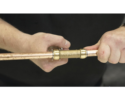 Une personne connecte un tube en cuivre avec un connecteur.