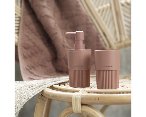 Seifenspender und Zahnputzbecher aus Keramik auf einem Rattantisch