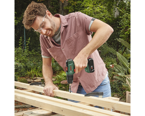 Un homme perce une planche de bois avec une perceuse-visseuse sans fil