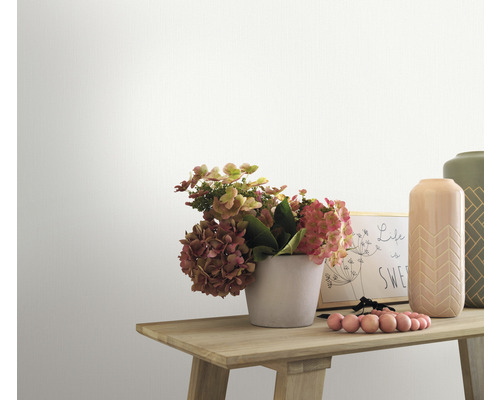 Nahaufnahme eines dekorierten Holztisches mit Blumen, Vasen und einem Bilderrahmen vor einer weißen Wand