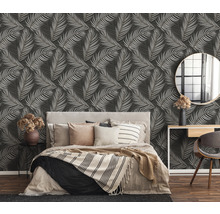 Chambre avec lit devant un mur avec du papier peint à motifs de feuilles.