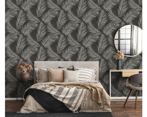 Chambre avec lit devant un mur avec du papier peint à motifs de feuilles.