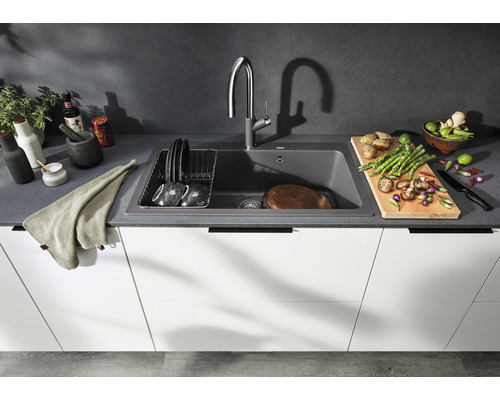 Küchenszene mit Spüle, Armatur, Geschirr und Lebensmitteln auf einer Arbeitsfläche.