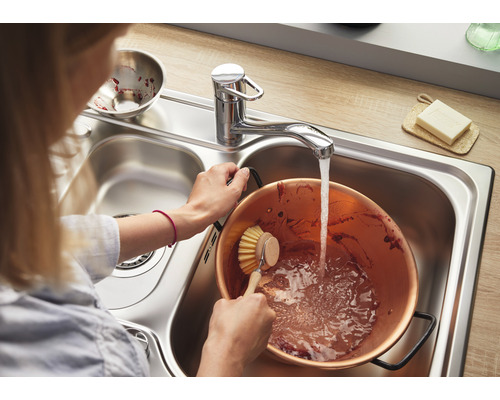 Frau spült Kupfertopf in einer Edelstahlspüle mit Wasserhahn.