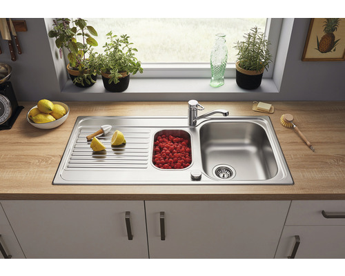 Évier en acier inoxydable avec égouttoir et bac rempli de framboises sur un plan de travail de cuisine