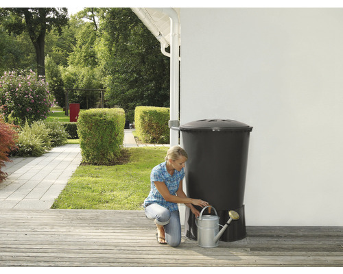 Femme remplissant un arrosoir à un récupérateur d''eau de pluie dans un jardin