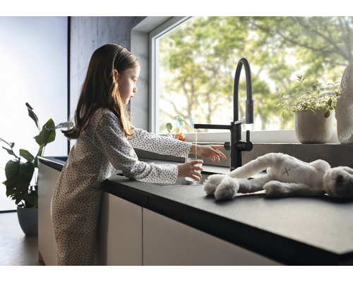 Mädchen füllt ein Glas Wasser an einem schwarzen Küchenarmatur