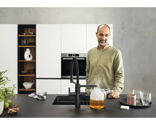 Cuisine moderne avec robinetterie noire, évier et un homme regardant une carafe en verre avec de l''eau chaude.