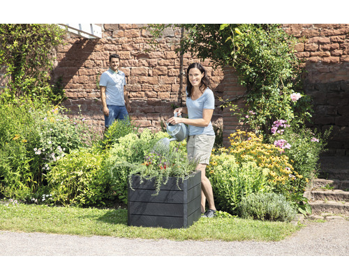 "Frau giesst Pflanzen in einem schwarzen Pflanzkasten im Garten
