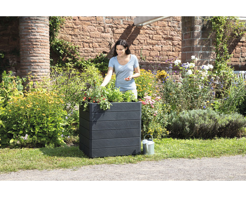 Frau gärtnert in einem schwarzen Pflanzkasten im Garten