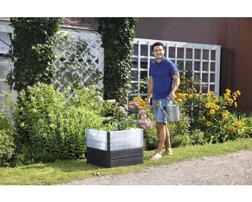 Hochbeet mit Blumen und Mann mit Gießkanne im Garten