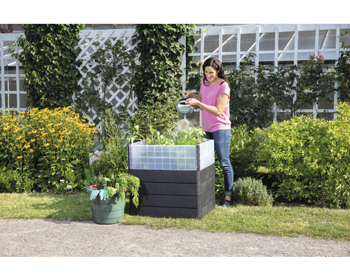 Femme arrosant des plantes dans un potager surélevé en plastique dans le jardin.